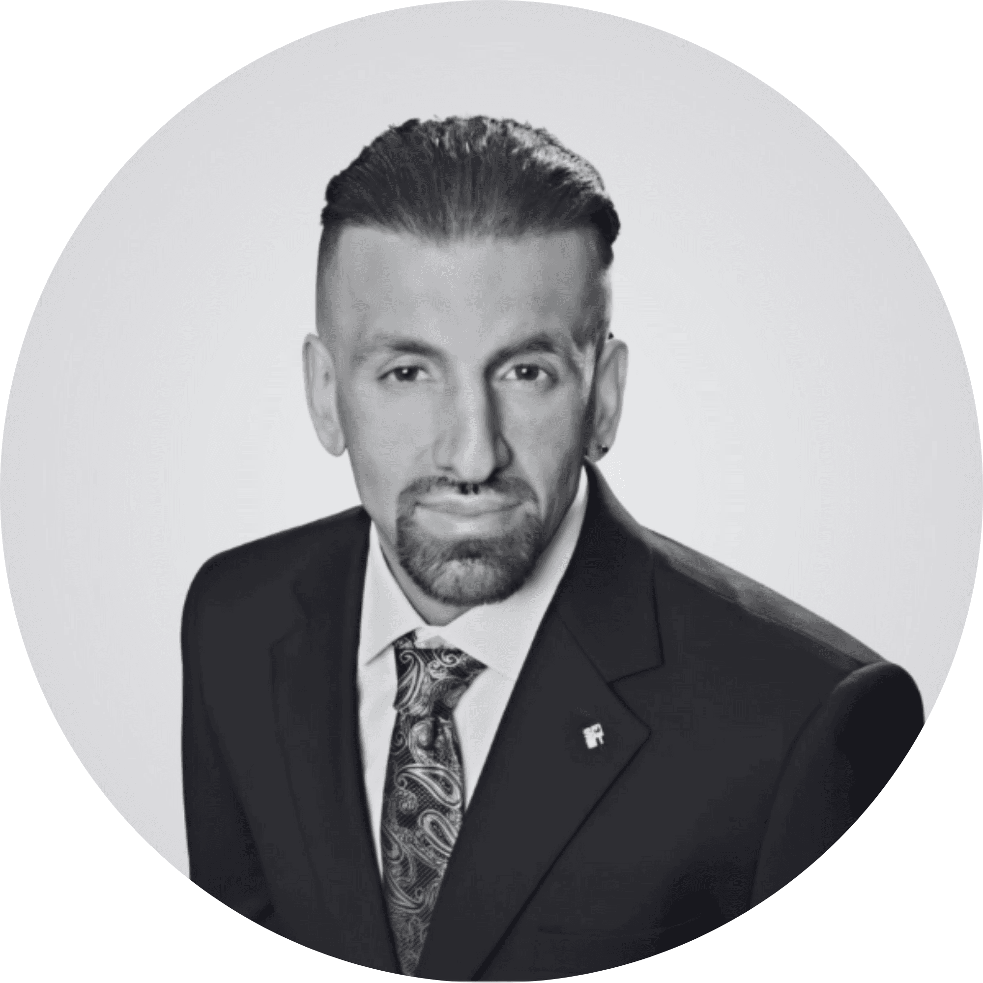 Professional black and white circular headshot of a man with a goatee and paisley tie.