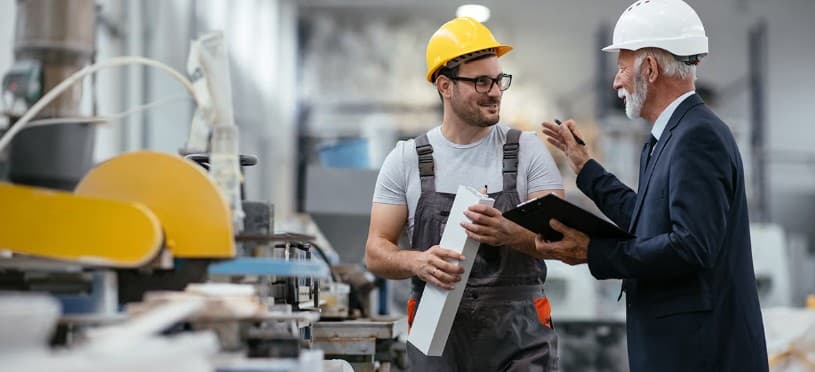 Senior manager in a suit and a factory worker in hard hats discussing production.