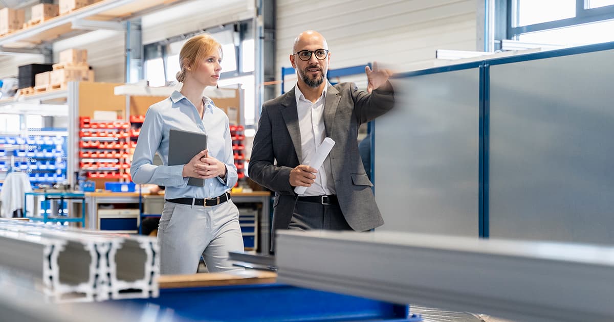 Two professionals in business attire walk through a modern manufacturing facility discussing production details.